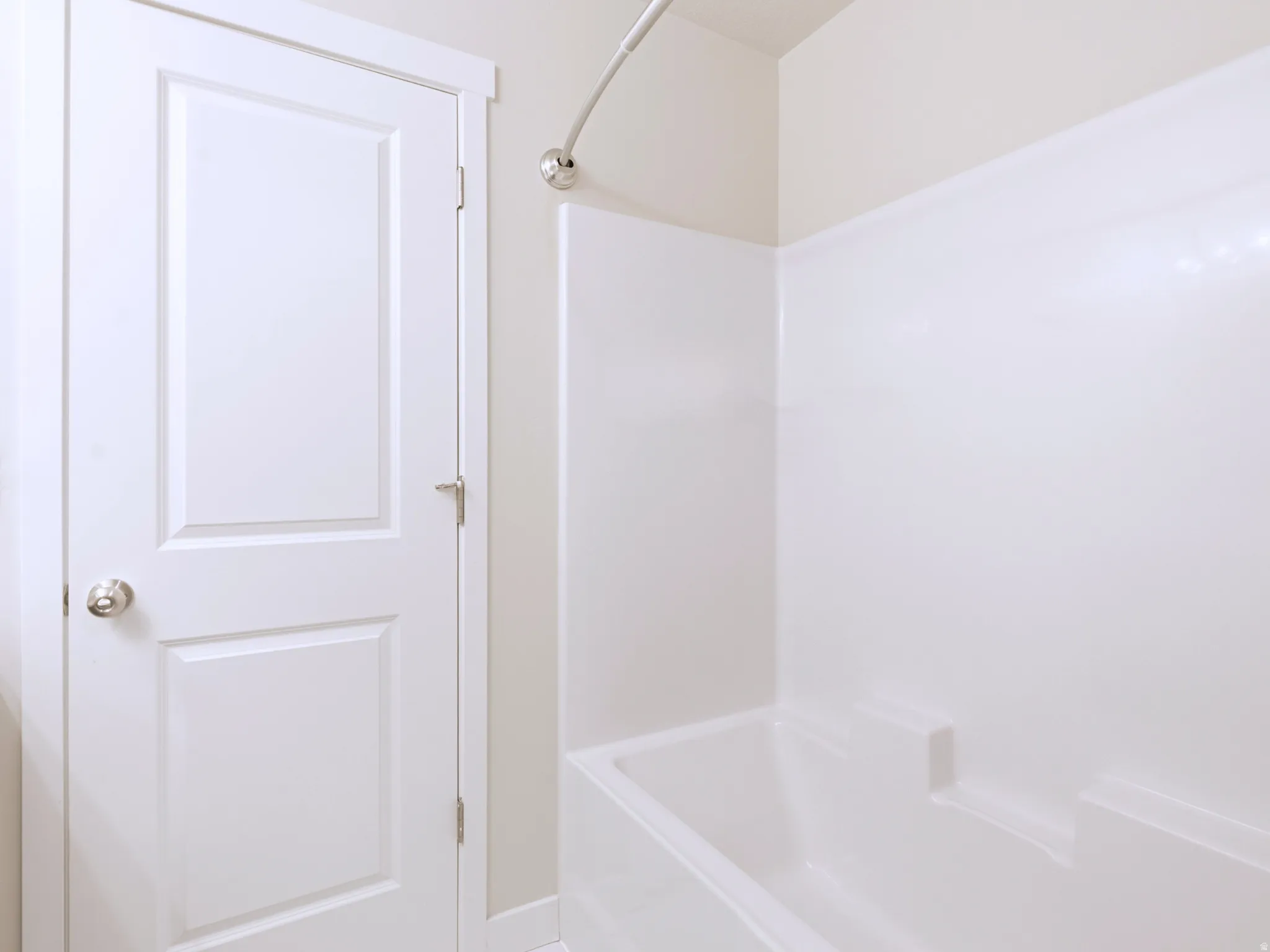 Built-in bathtub with integrated shelving, chrome shower fixture, and a paneled door with a round knob