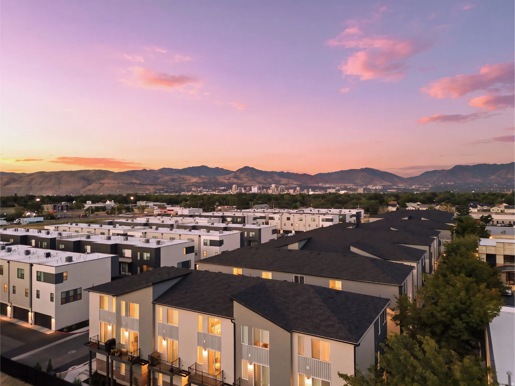 Modern residential development featuring multiple-story townhomes with balconies, surrounded by mature trees
