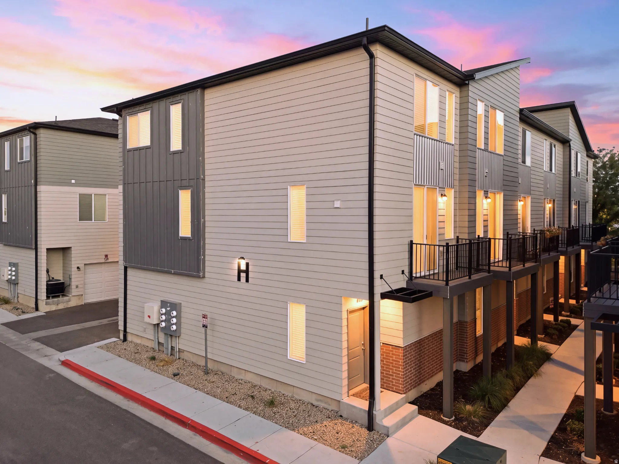 Modern exterior with horizontal siding, vertical paneling, brick accents, and multiple balconies with dark railings