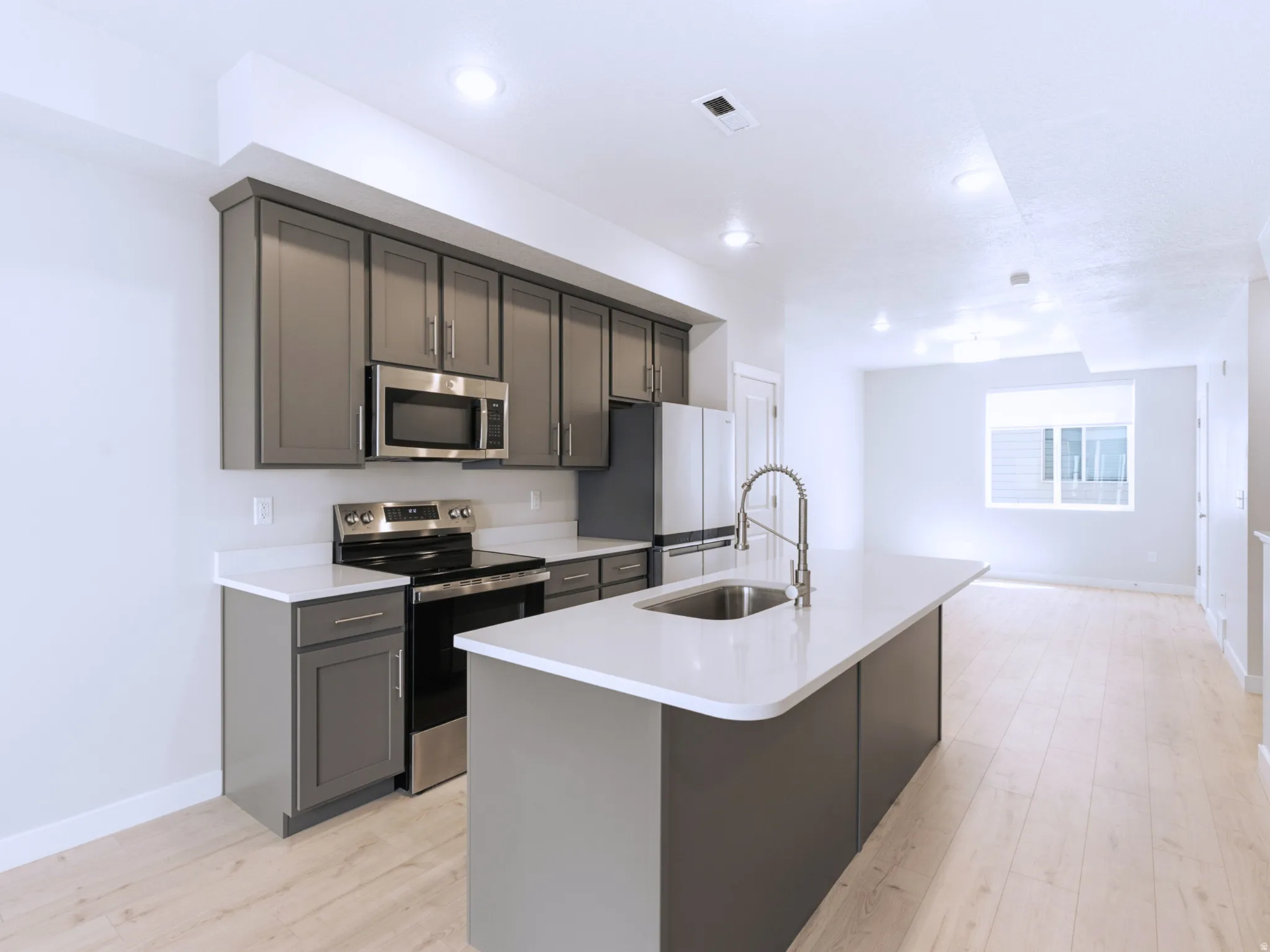 Modern kitchen featuring gray cabinetry, stainless steel appliances, white countertops, and a center island with a sink