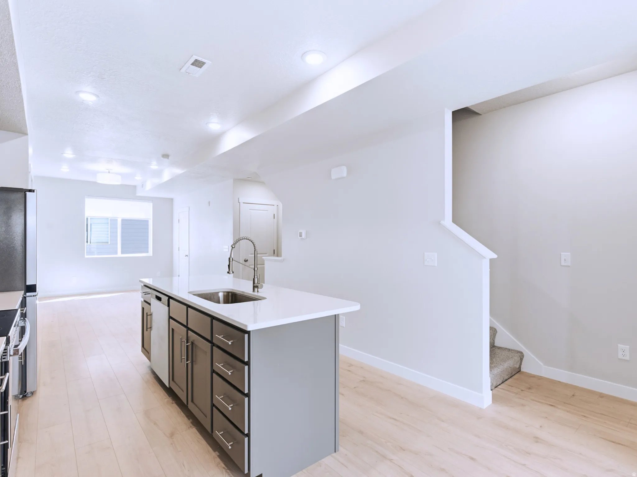 Kitchen island with integrated sink, stainless steel appliances, light wood-finish flooring, recessed lighting, and a stairway with carpeted steps