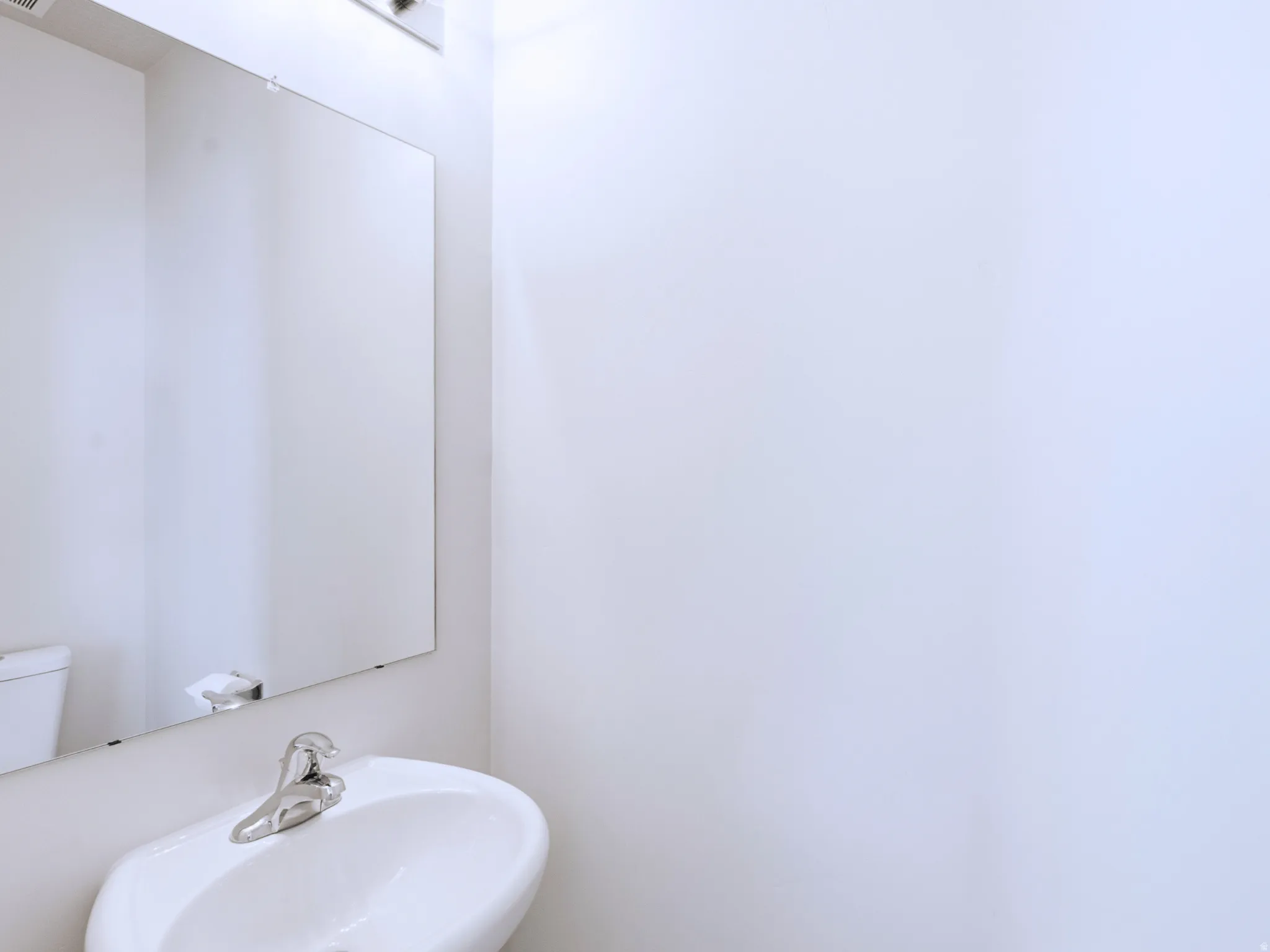 Wall-mounted mirror over a white ceramic pedestal sink with a chrome faucet