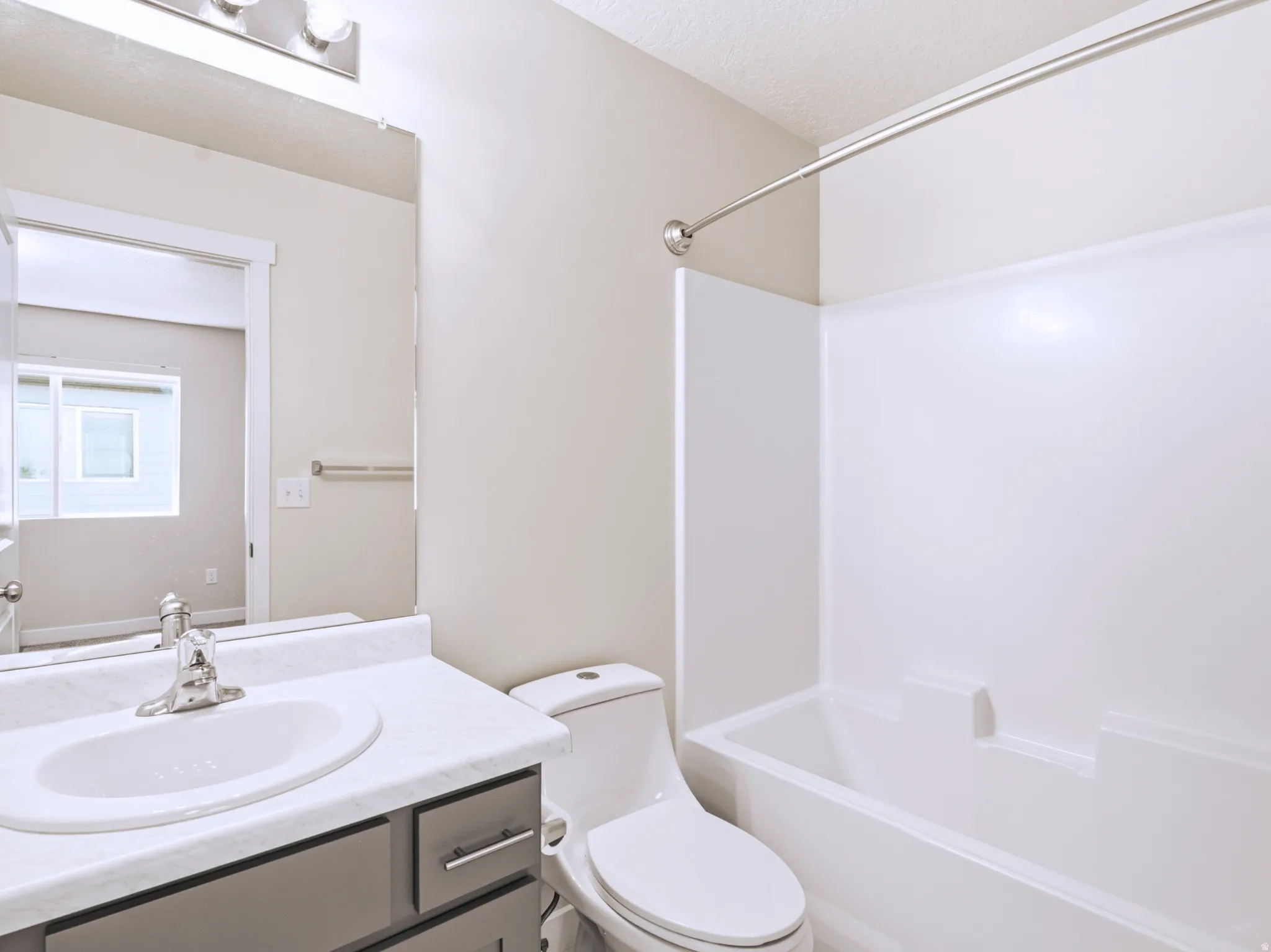 White bathtub and shower surround, vanity with an integrated sink, polished chrome faucet, and gray cabinetry with brushed nickel hardware