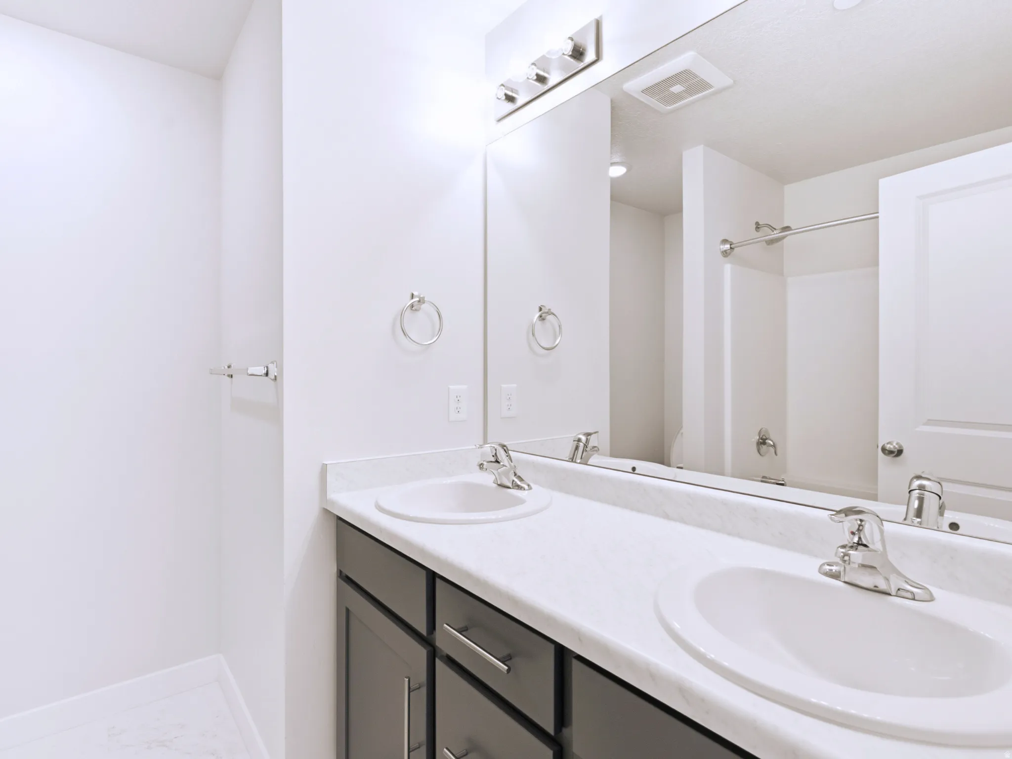 Dual undermount sinks with chrome fixtures, dark wood-finish vanity with chrome pulls, expansive vanity mirror with overhead light fixture, and white walls