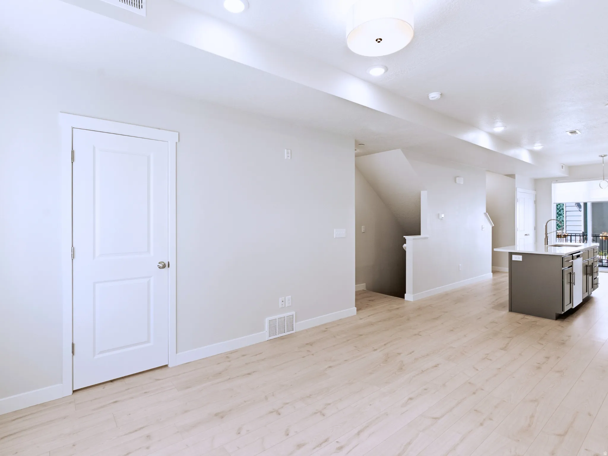 Light wood-finish flooring, recessed lighting, white interior door, contemporary ceiling light fixture, and a gray kitchen island with a sink