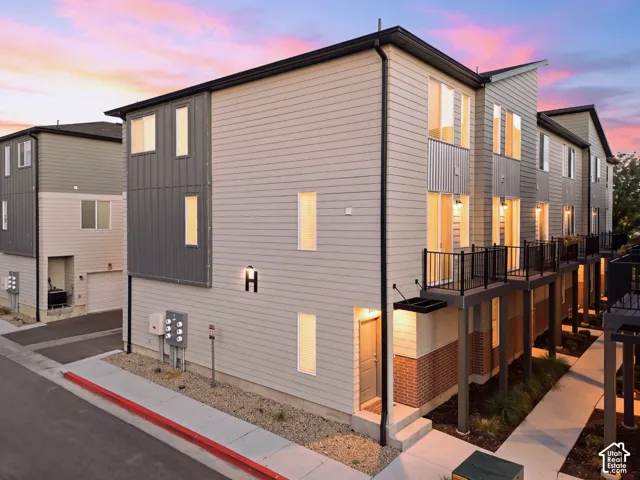 Modern exterior featuring light-toned siding, dark metal accents, multiple balconies with black railings, a sloped roofline, and visible entryways
