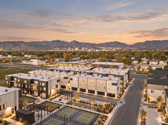 Multi-level townhome community featuring contemporary exterior siding, two dedicated pickleball courts, pergola-covered outdoor seating areas, and mountain and city skyline backdrops