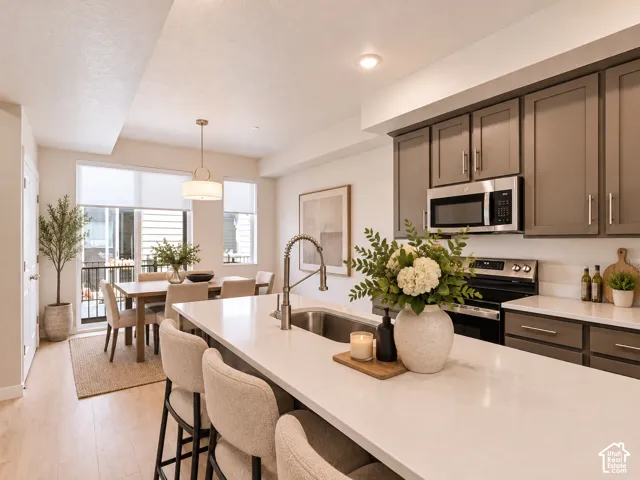 Kitchen featuring solid-surface countertops, an undermount sink with a gooseneck faucet, gray shaker-style cabinetry, stainless steel appliances, and wood-finish flooring