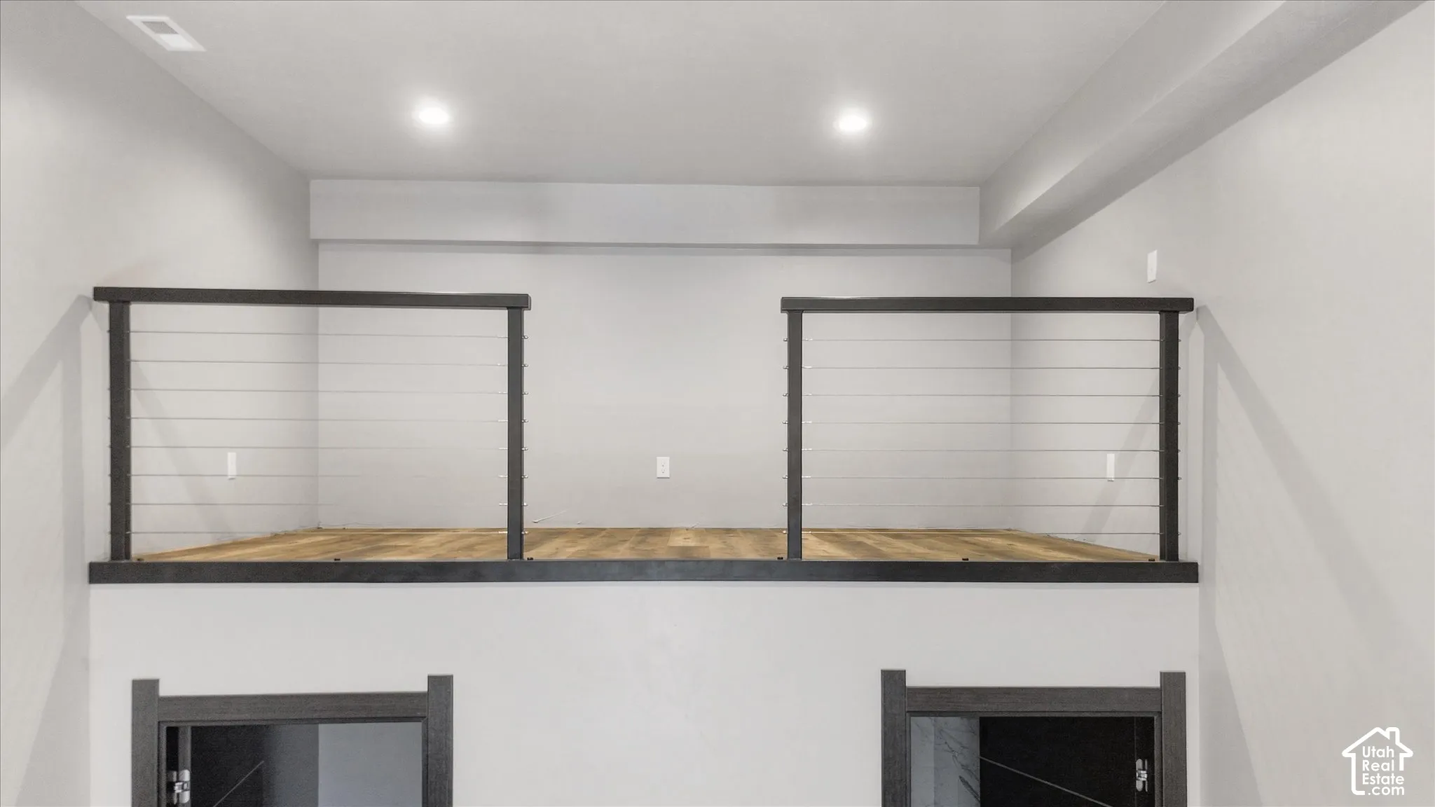 Modern lofted spaces feature black-framed railing systems with horizontal cable design, wood-finish flooring, and recessed ceiling lighting