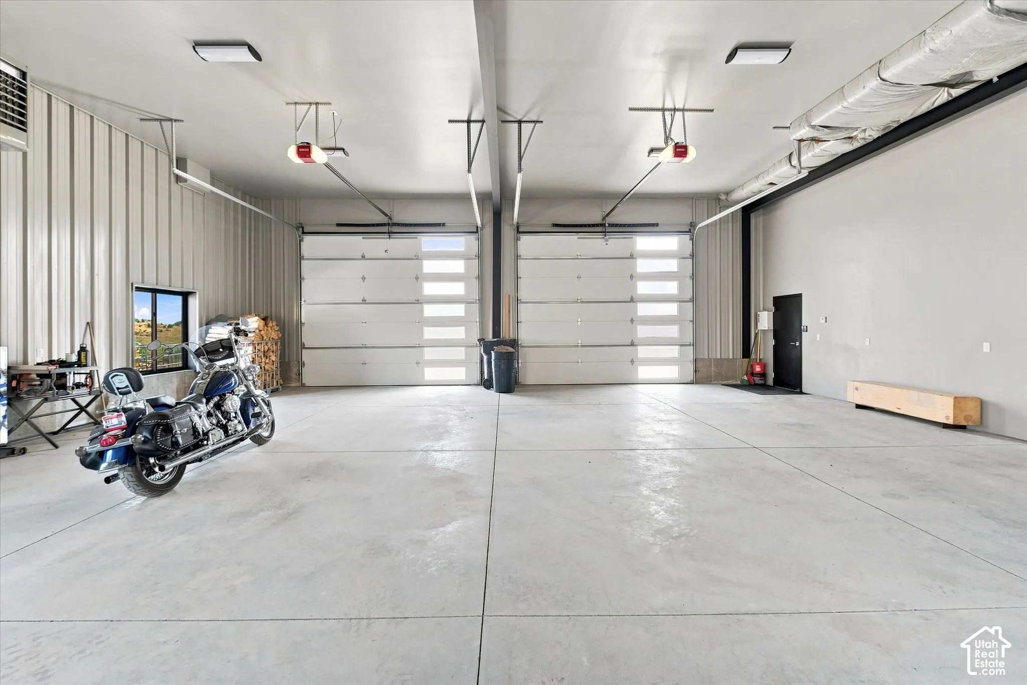 Spacious garage featuring two overhead doors with frosted glass panels, concrete flooring, exposed metal wall paneling, and an interior window