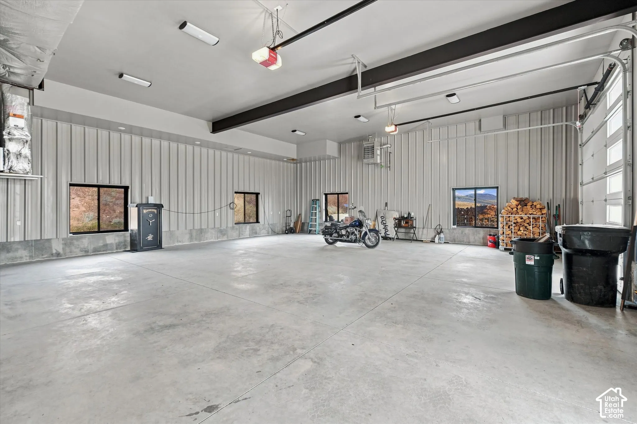 Spacious interior with high ceilings, multiple windows, exposed structural beams, and a large garage door