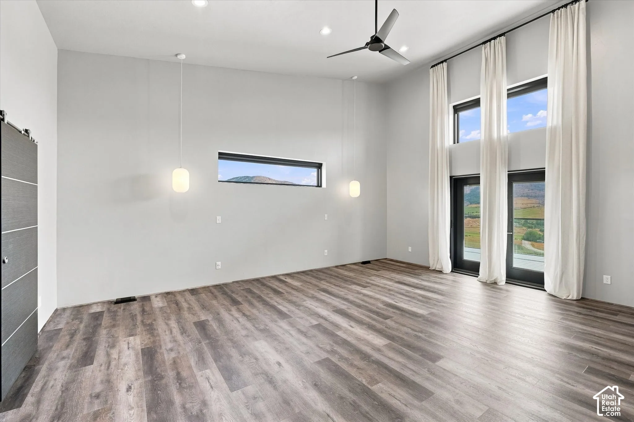 Spacious room showcasing wide-plank wood-finish flooring, recessed ceiling lighting, and a ceiling fan