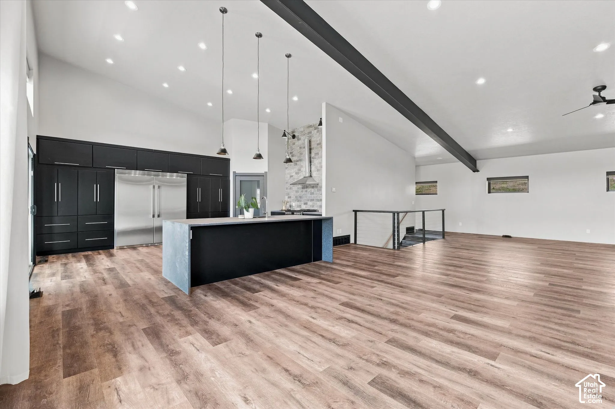 Vaulted ceilings with exposed beam, wood-finish flooring, modern kitchen with integrated appliances, kitchen island with pendant lighting, and metal railing staircase