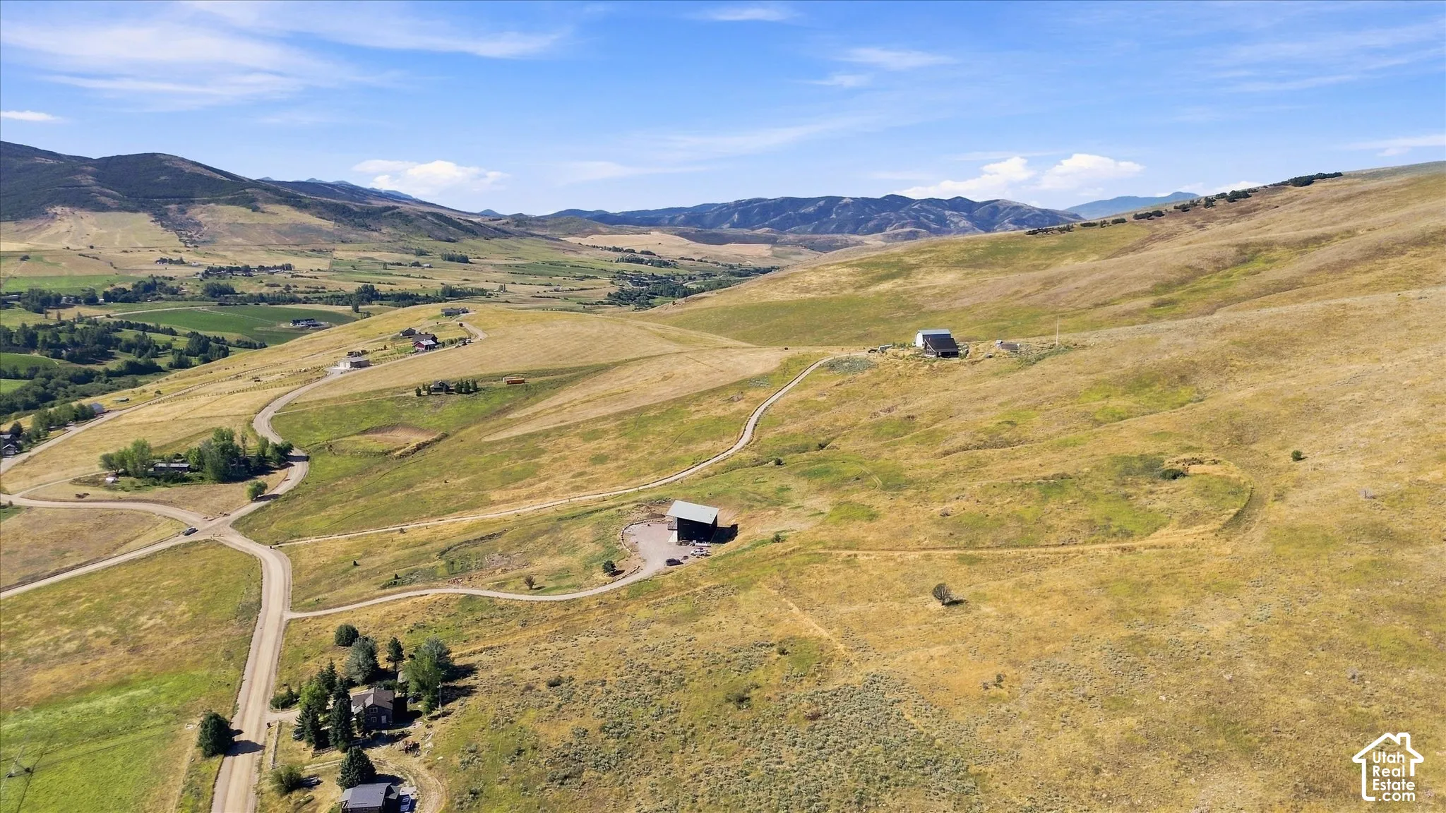 Expansive rural acreage with multiple structures, winding dirt roads, and distant mountainous terrain