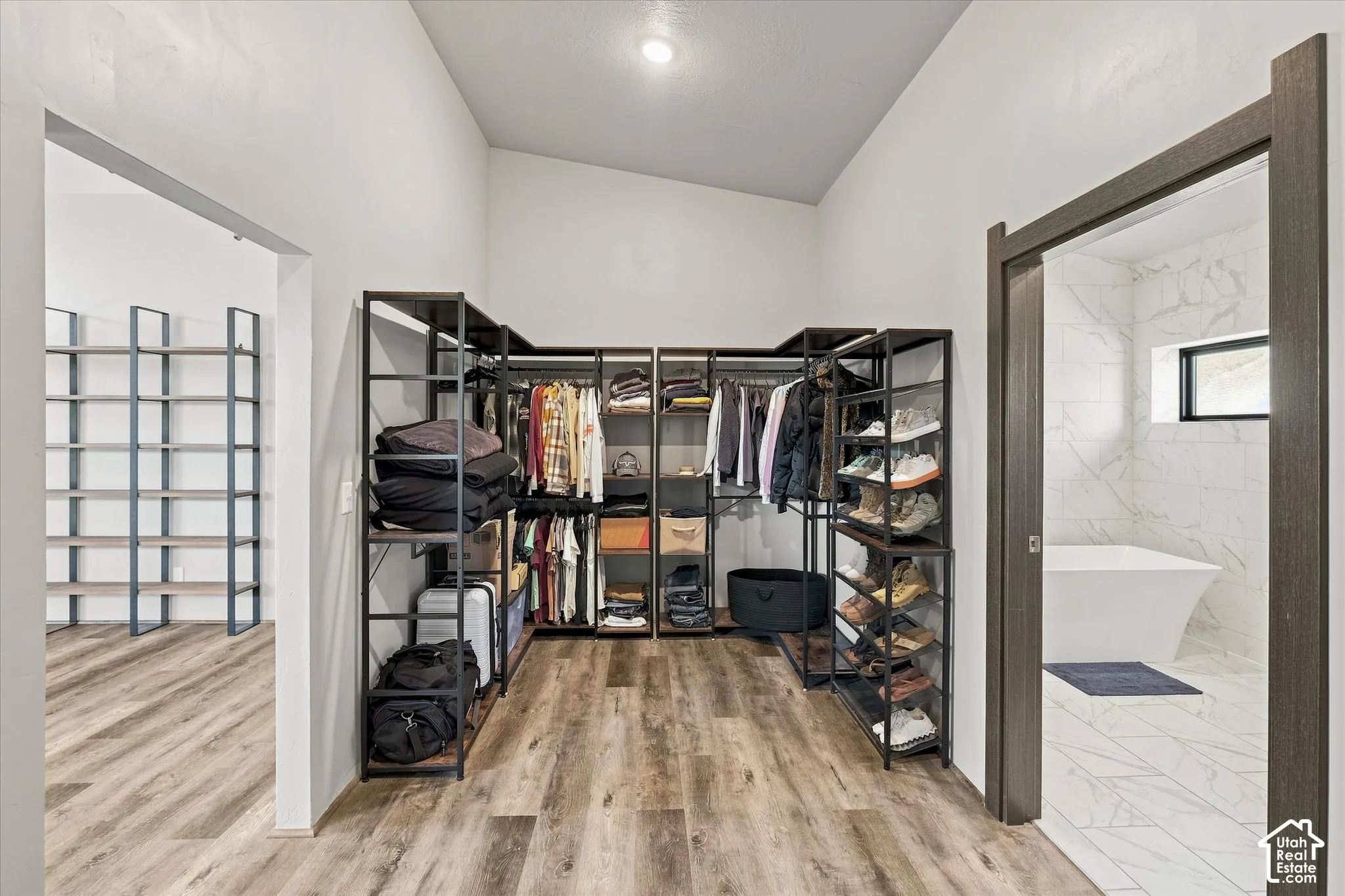 Spacious walk-in closet featuring custom black metal shelving and clothing rods, wood-finish flooring, and abundant storage capacity with organized compartments for apparel and accessories
