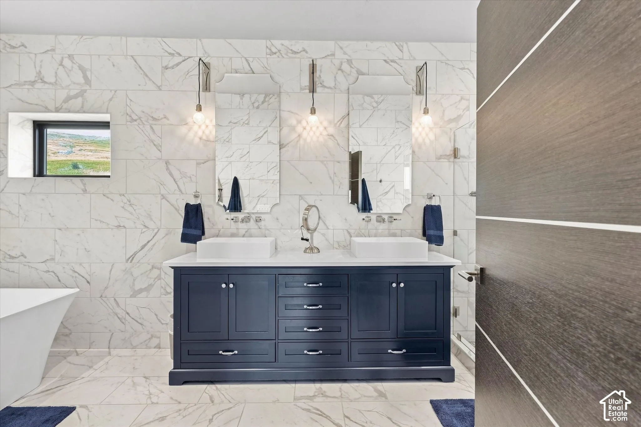 Luxurious dual-vanity bathroom featuring a navy blue cabinetry base with ample storage, polished stone countertops, and chrome fixtures