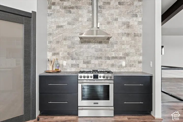 Contemporary kitchen featuring stainless steel range with dual ovens and cooktop, black cabinetry with polished chrome hardware, quartz countertops, and a geometric tile backsplash in neutral tones