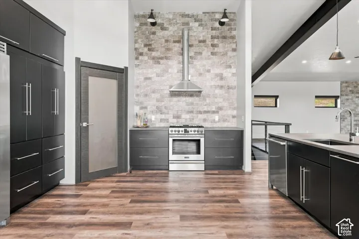 Gourmet kitchen with wood-finish flooring, dark cabinetry, stainless steel appliances, and a brick-finish accent wall