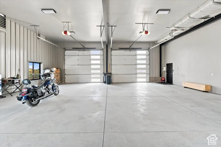 Spacious garage featuring two overhead doors with frosted glass panels, concrete flooring, exposed metal wall paneling, and an interior window