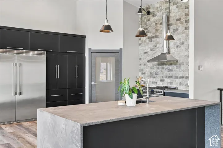 Stainless steel refrigerator and range with hood, dark cabinetry, light-toned brick-look backsplash, and a kitchen island with an integrated sink