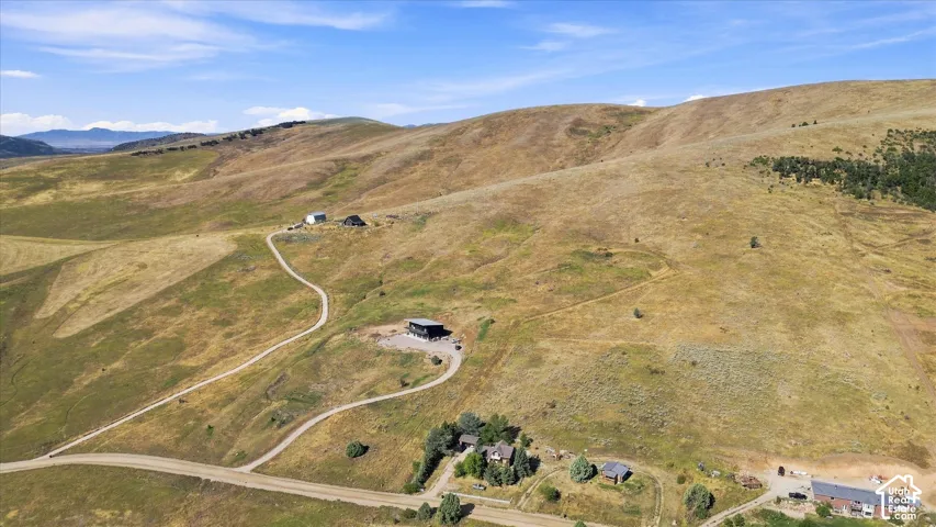 Expansive hillside property featuring multiple buildings, winding unpaved roads, natural terrain, and distant mountain ranges