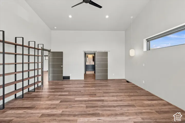 Vaulted ceiling with a ceiling fan, wood-finish flooring, built-in shelving, horizontal window, and sliding barn doors