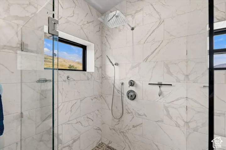Walk-in shower with tile surround, glass enclosure, rain showerhead, and a fixed window
