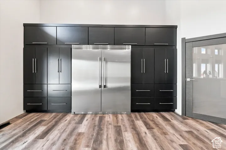 Stainless steel side-by-side refrigerator, extensive dark wood-finish cabinetry, wood-finish flooring, and a frosted glass-paneled interior door