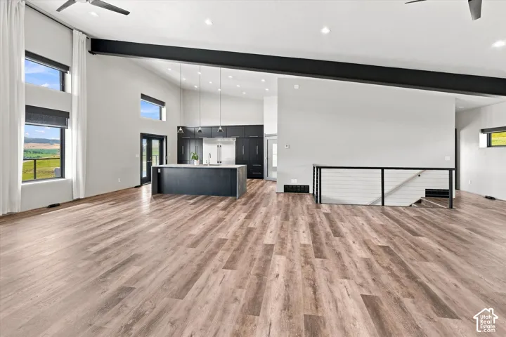 Vaulted ceiling with exposed beam, wood-finish flooring, modern kitchen island with white countertop, full-height windows, and black metal staircase railing
