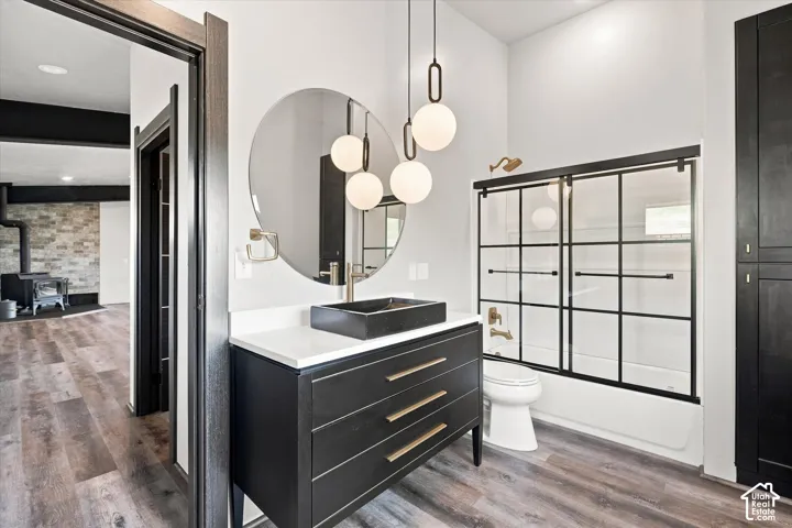 Modern bathroom featuring a rectangular vessel sink, white countertop, dark wood-finish vanity with gold-tone hardware, and a tub/shower combination with sliding glass doors