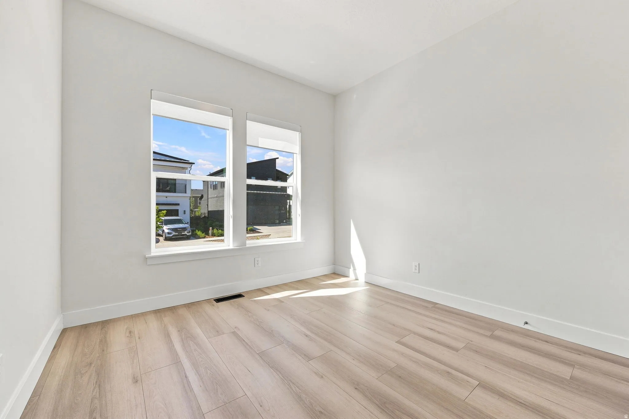 Light-filled room featuring two windows, wood-finish flooring, and white walls