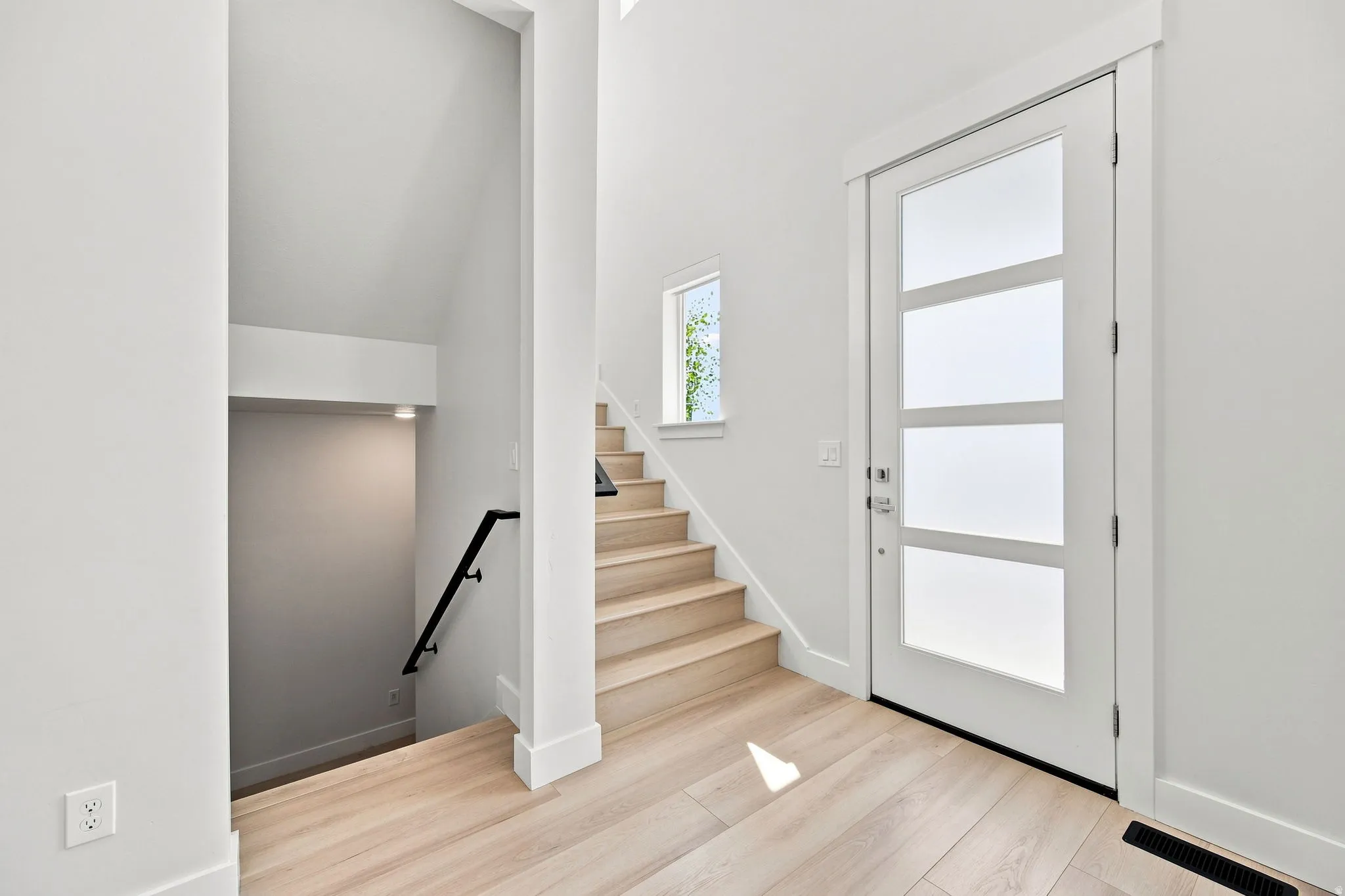 Entryway featuring a modern door with frosted glass panels, wood-finish flooring, and a contemporary staircase with a black handrail