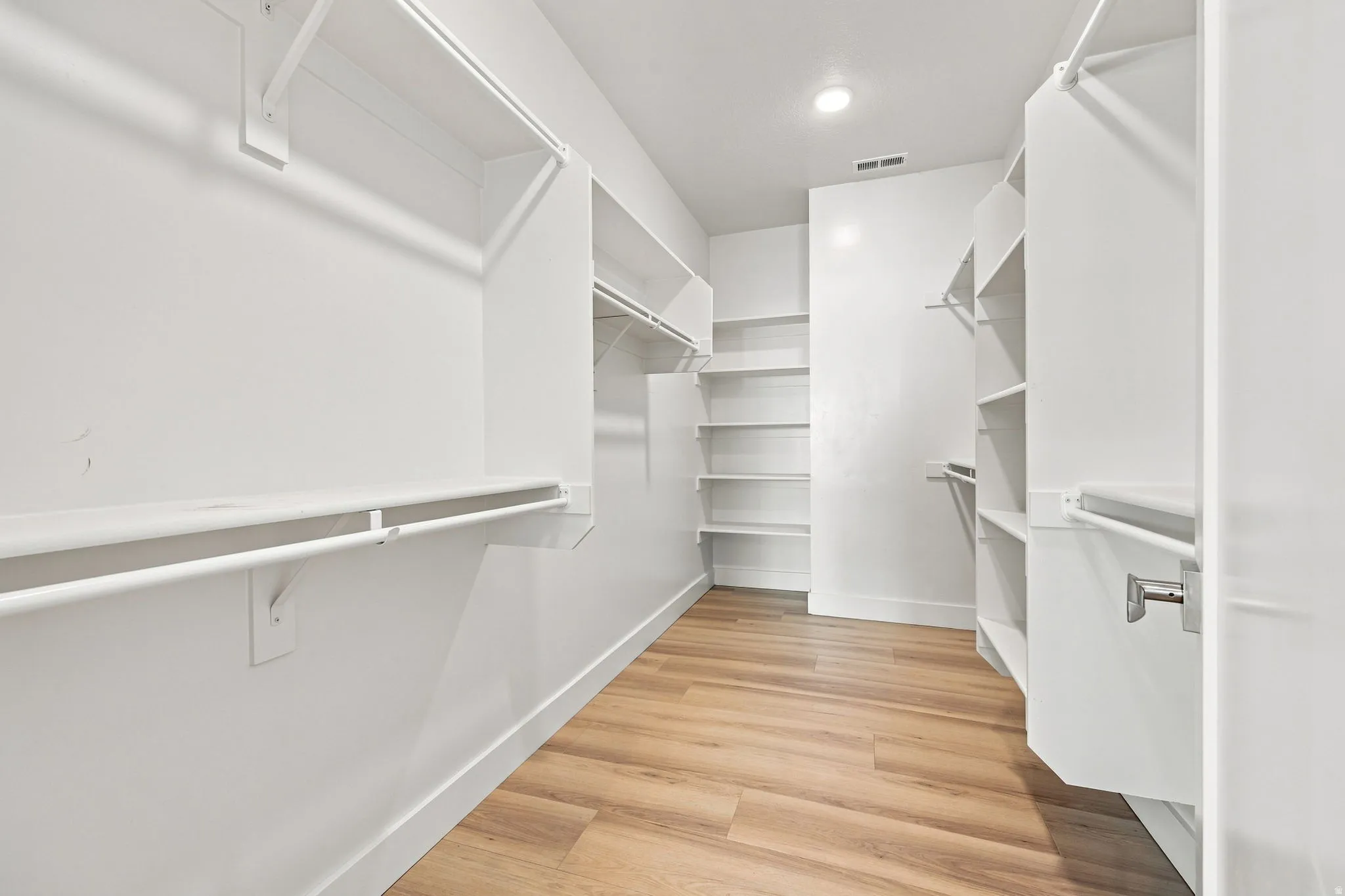Walk-in closet with wood-finish flooring, recessed lighting, multiple shelving units, and clothing rods