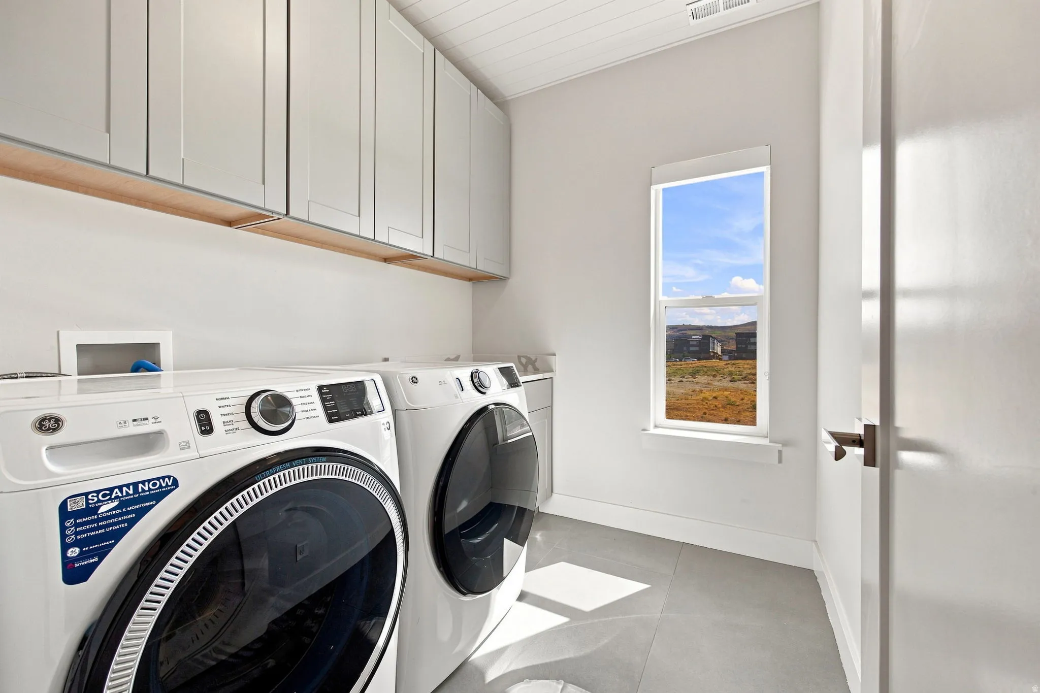 Laundry area featuring light gray cabinetry, a beadboard ceiling, and a large window