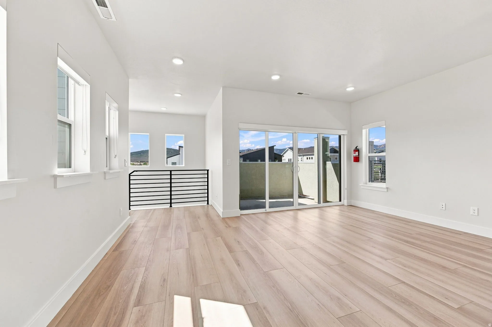 Light wood-finish flooring, recessed lighting, white walls, multiple windows, and sliding glass doors