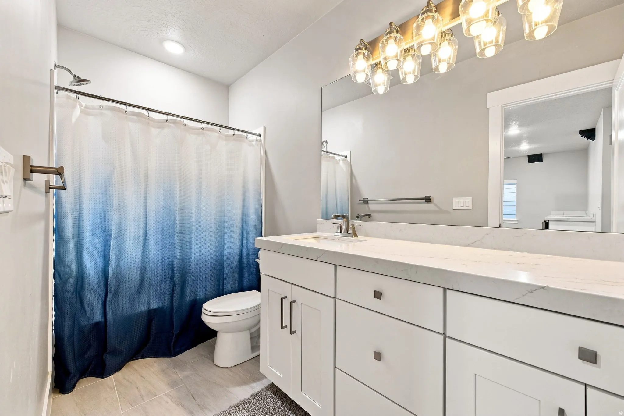 Full-size vanity mirror with a multi-bulb light fixture, white cabinetry with dark hardware, a white toilet, and a shower with a chrome fixture