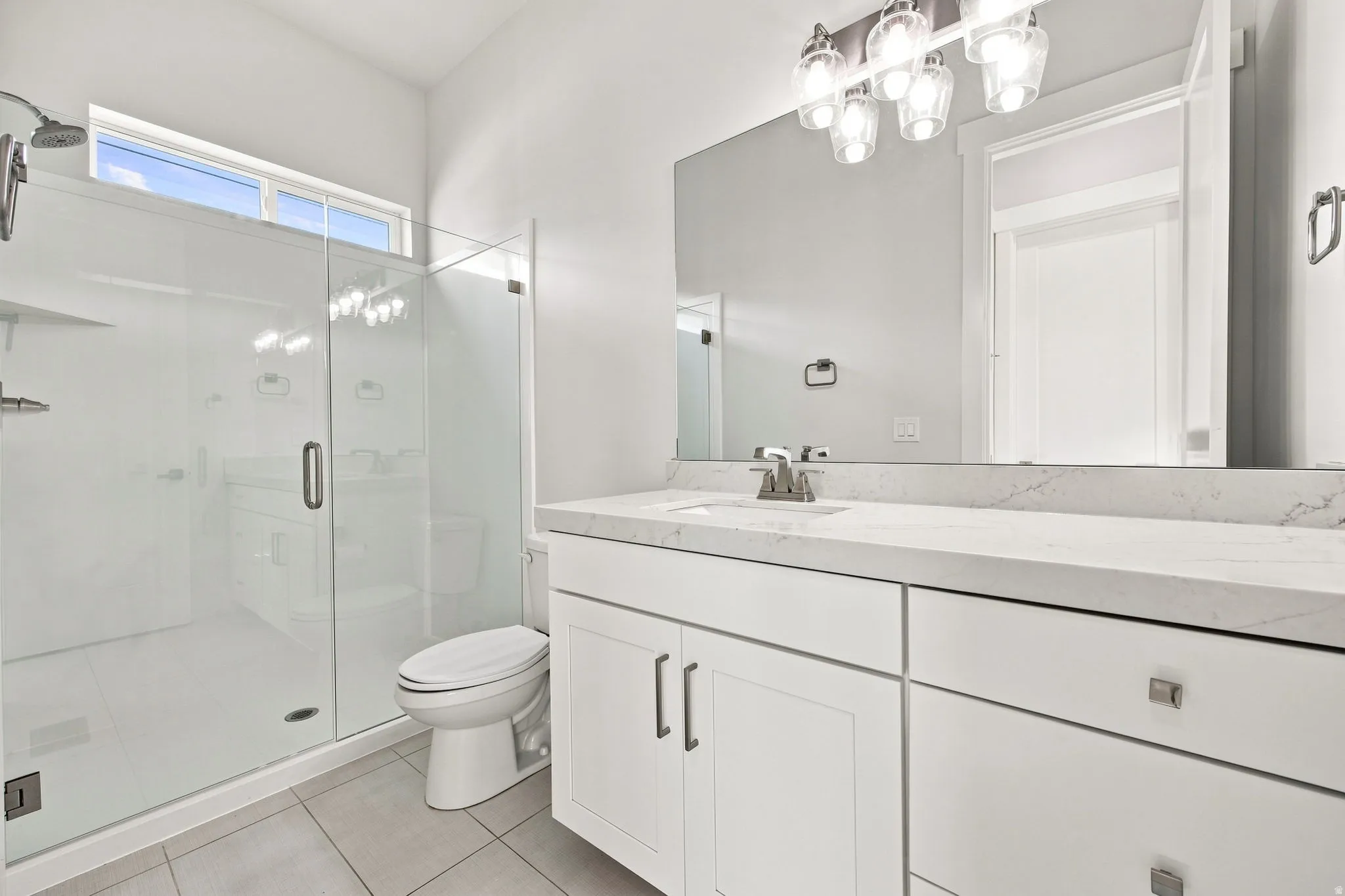 White vanity with a light-toned countertop, large mirror, and modern light fixture