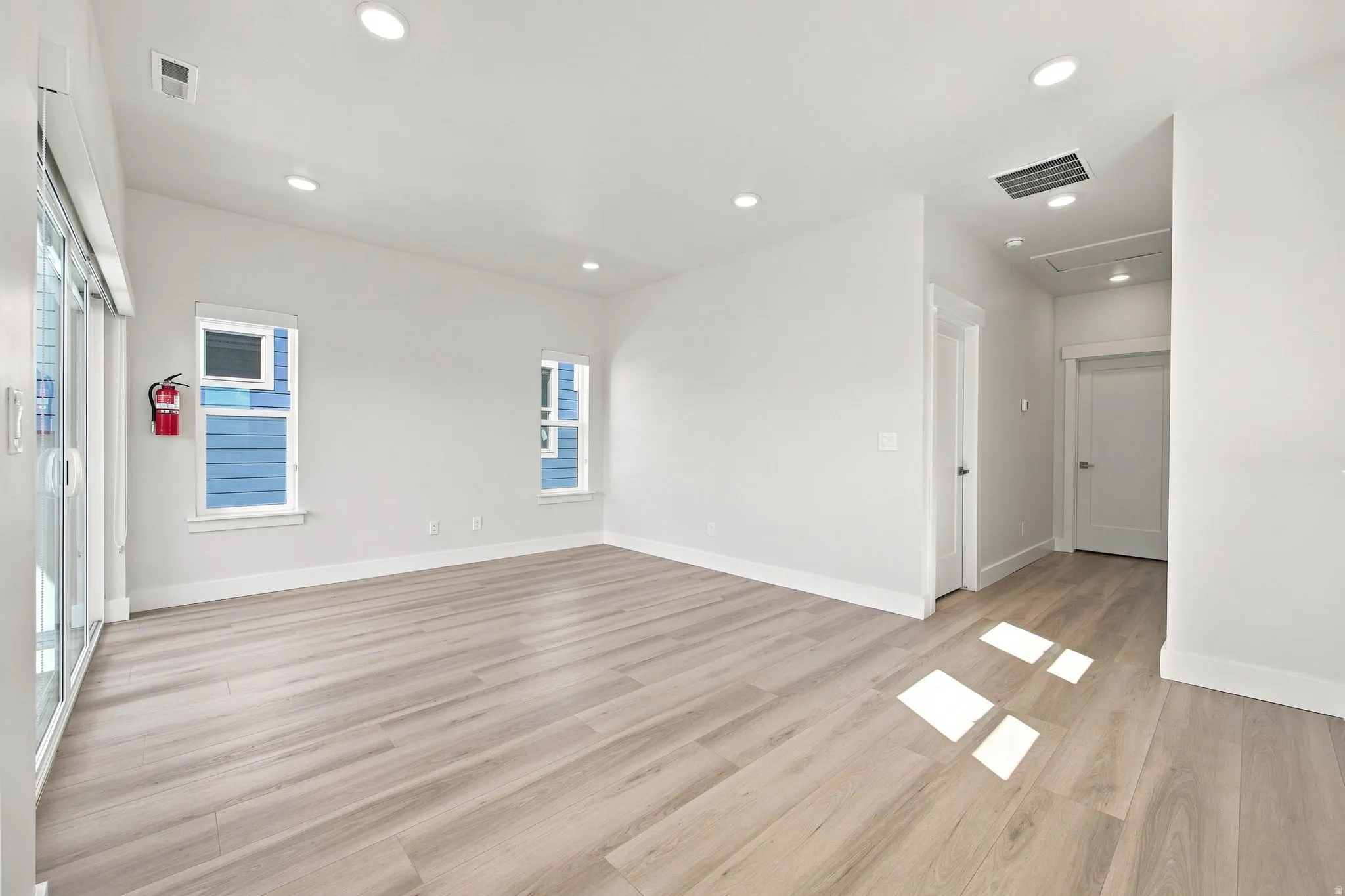 Spacious room featuring wood-finish flooring, recessed lighting, white walls, and bright windows
