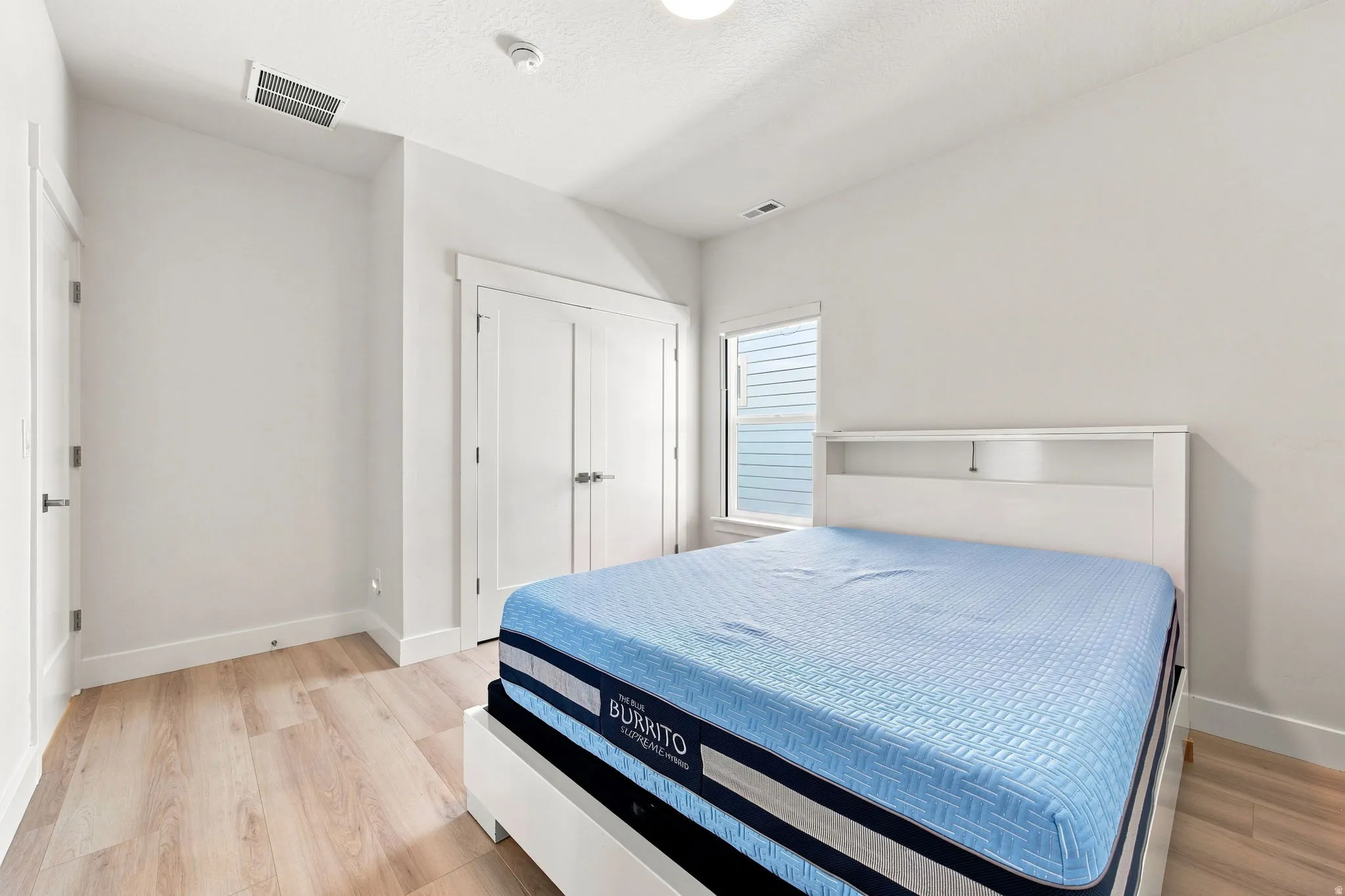 Light wood-finish flooring, white walls, double-door closet, and window with white trim