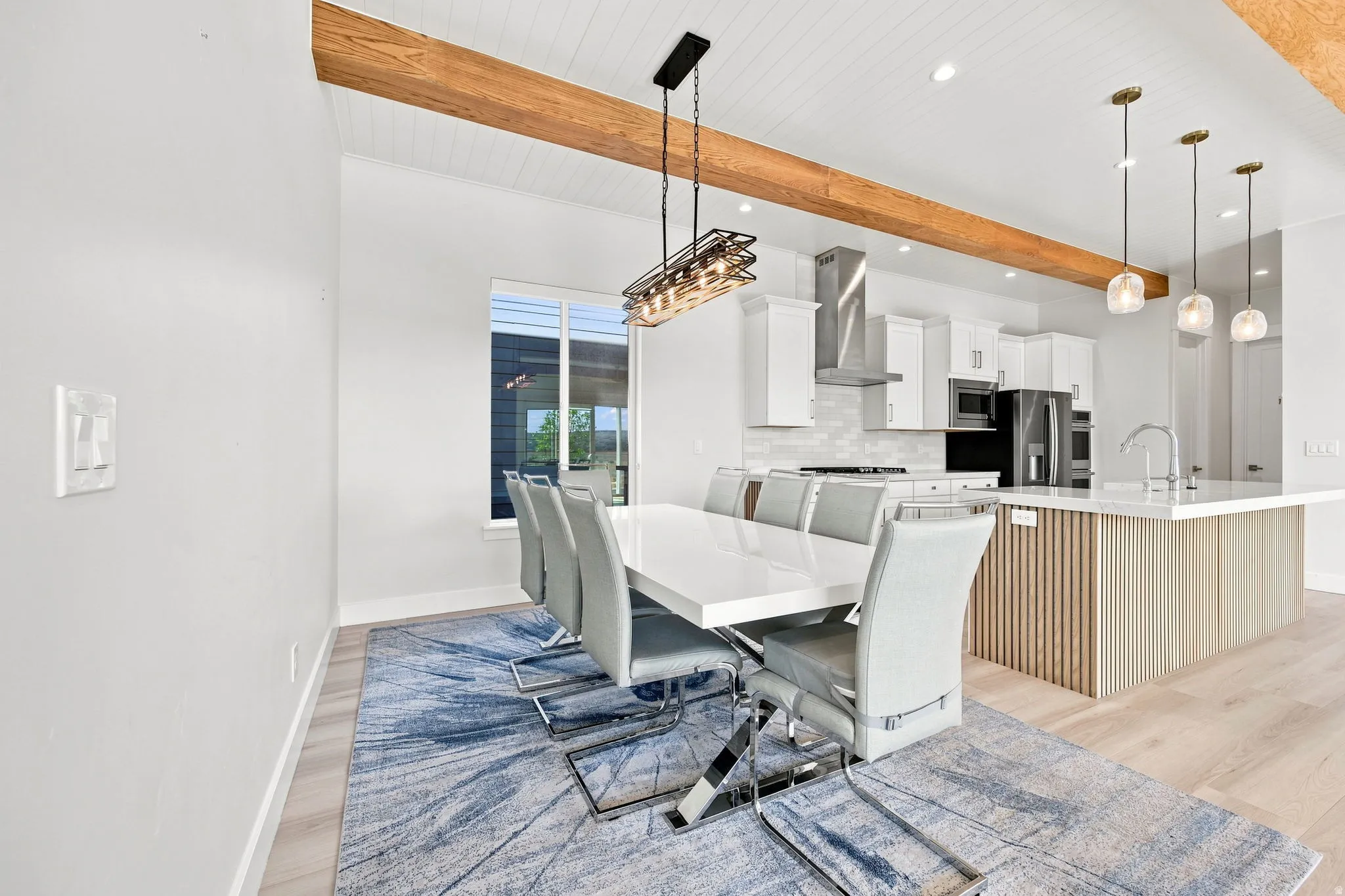 Open-concept dining and kitchen area featuring wood-finish flooring, a wood-beam ceiling, and white shaker cabinetry