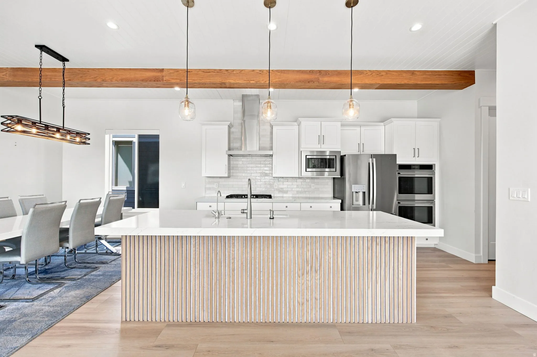 Kitchen island with reeded wood paneling and a light-toned countertop, stainless steel appliances, and wood-finish flooring