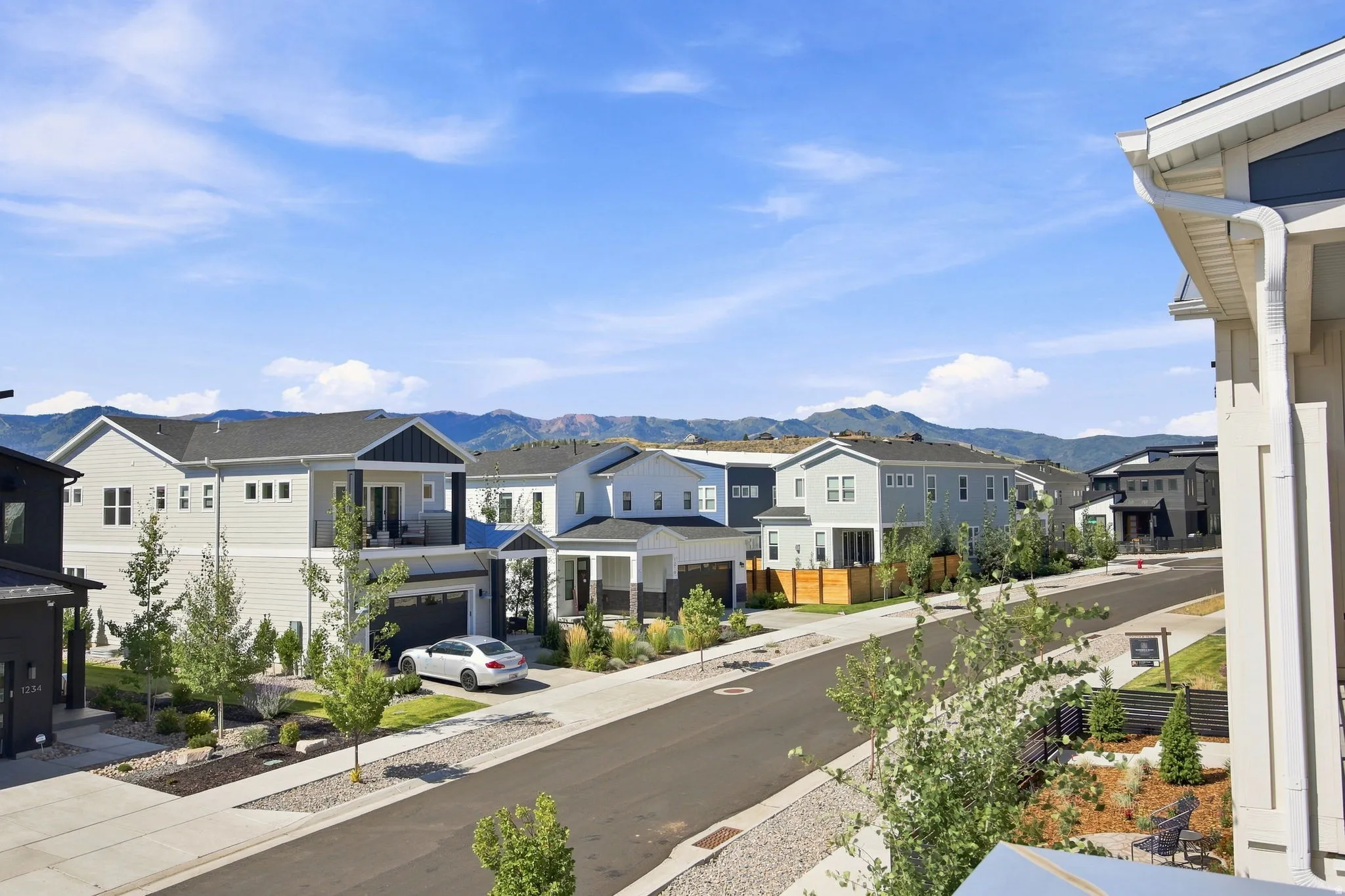 Newly developed residential street lined with contemporary homes featuring varied architectural styles, manicured landscaping, and mature plantings