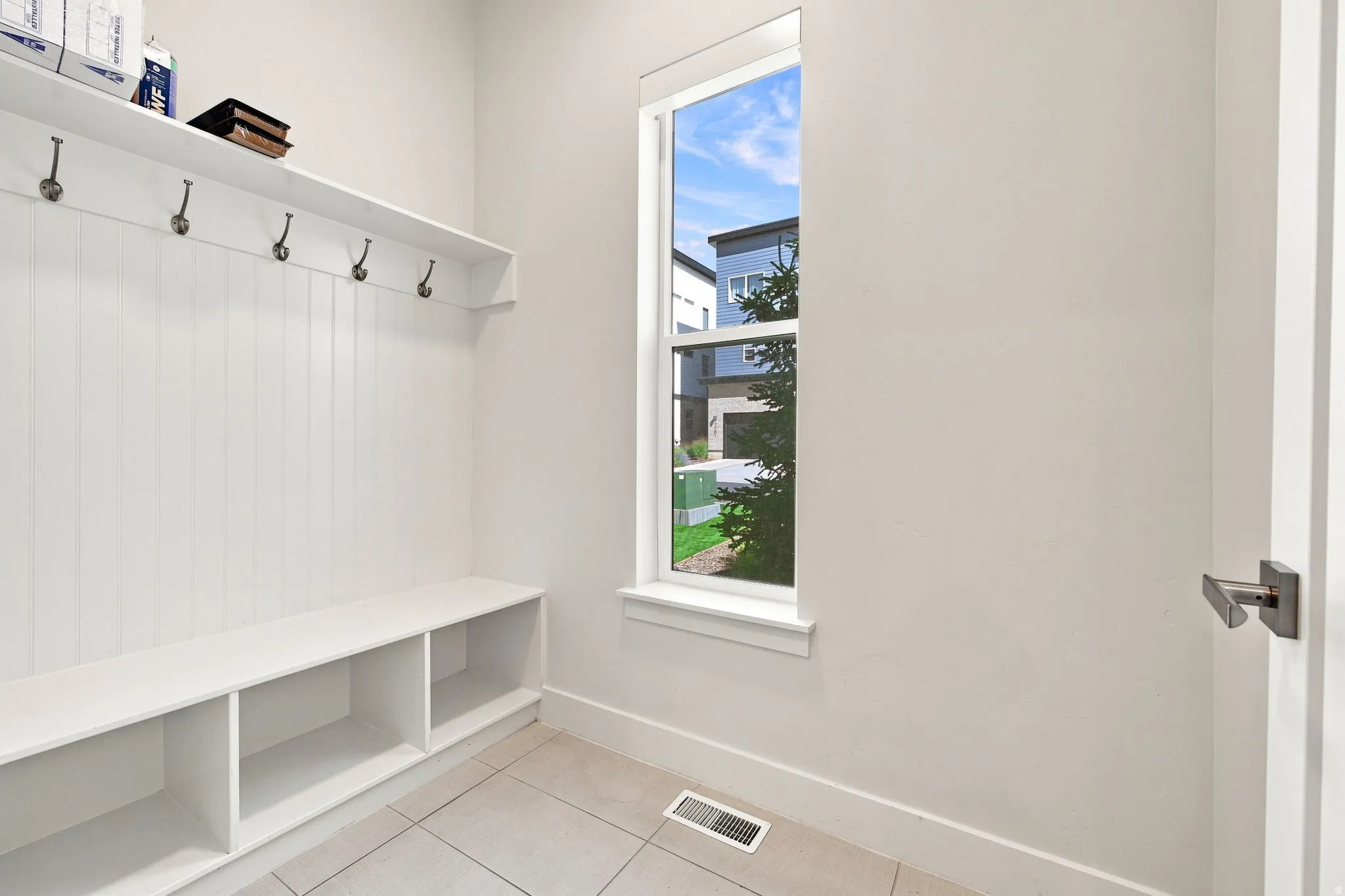 Built-in bench with cubby storage, upper shelf with hooks, single-pane window, and tile flooring