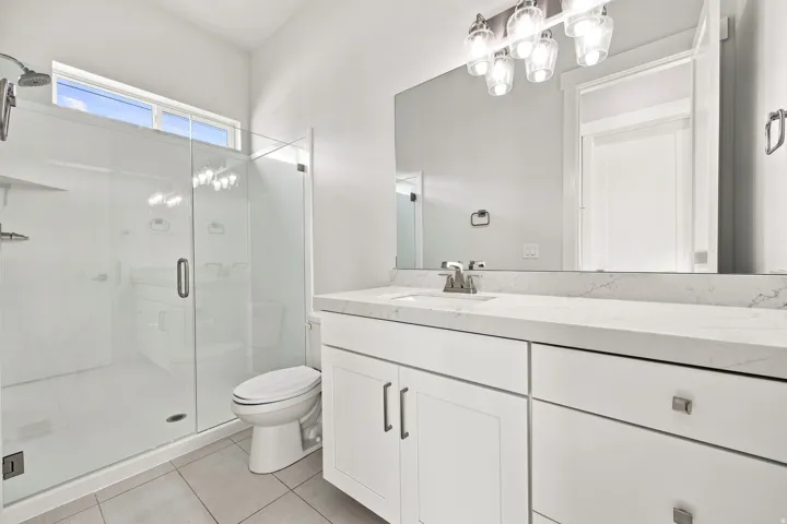 White vanity with a light-toned countertop, large mirror, and modern light fixture