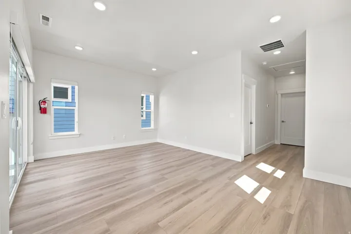 Spacious room featuring wood-finish flooring, recessed lighting, white walls, and bright windows