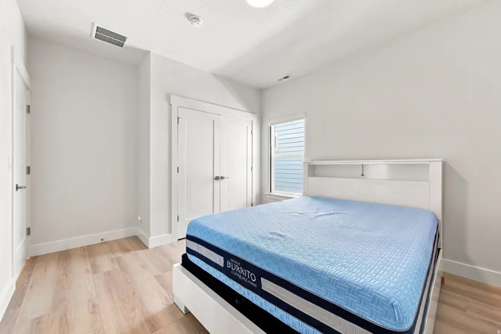 Light wood-finish flooring, white walls, double-door closet, and window with white trim