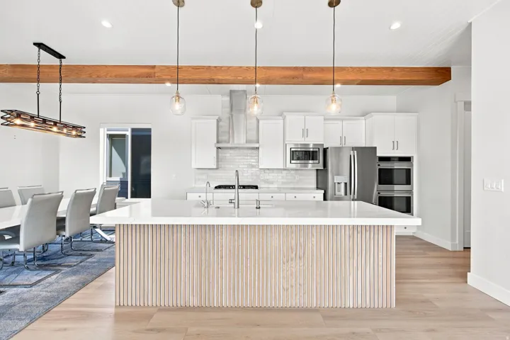 Kitchen island with reeded wood paneling and a light-toned countertop, stainless steel appliances, and wood-finish flooring