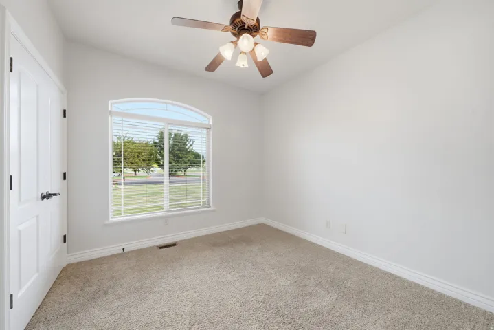 Arched window with ceiling fan and neutral carpeting.