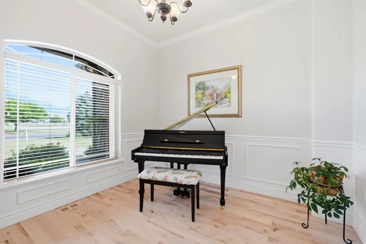 Arched window with blinds, light hardwood-finish flooring, white wall paneling, and crown molding