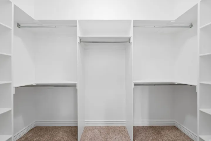 Primary closet Built-in white shelving, multiple hanging rods, and carpeted flooring